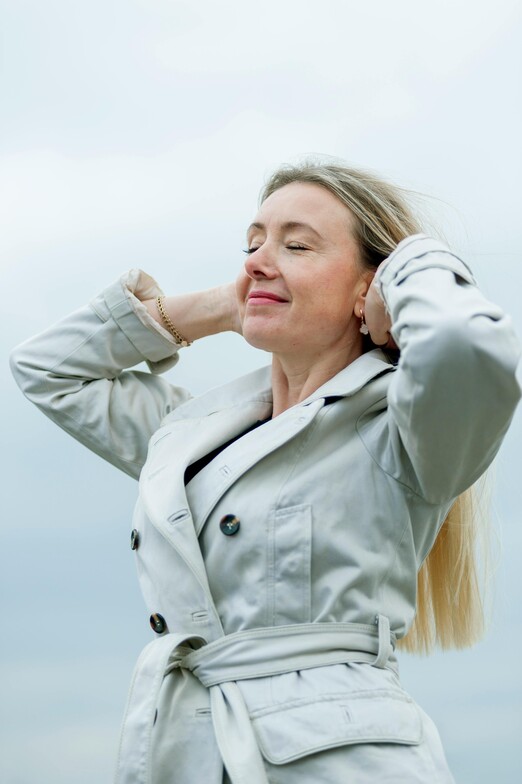 Woman standing outdoors with eyes closed, appearing calm , grounded and happy.
